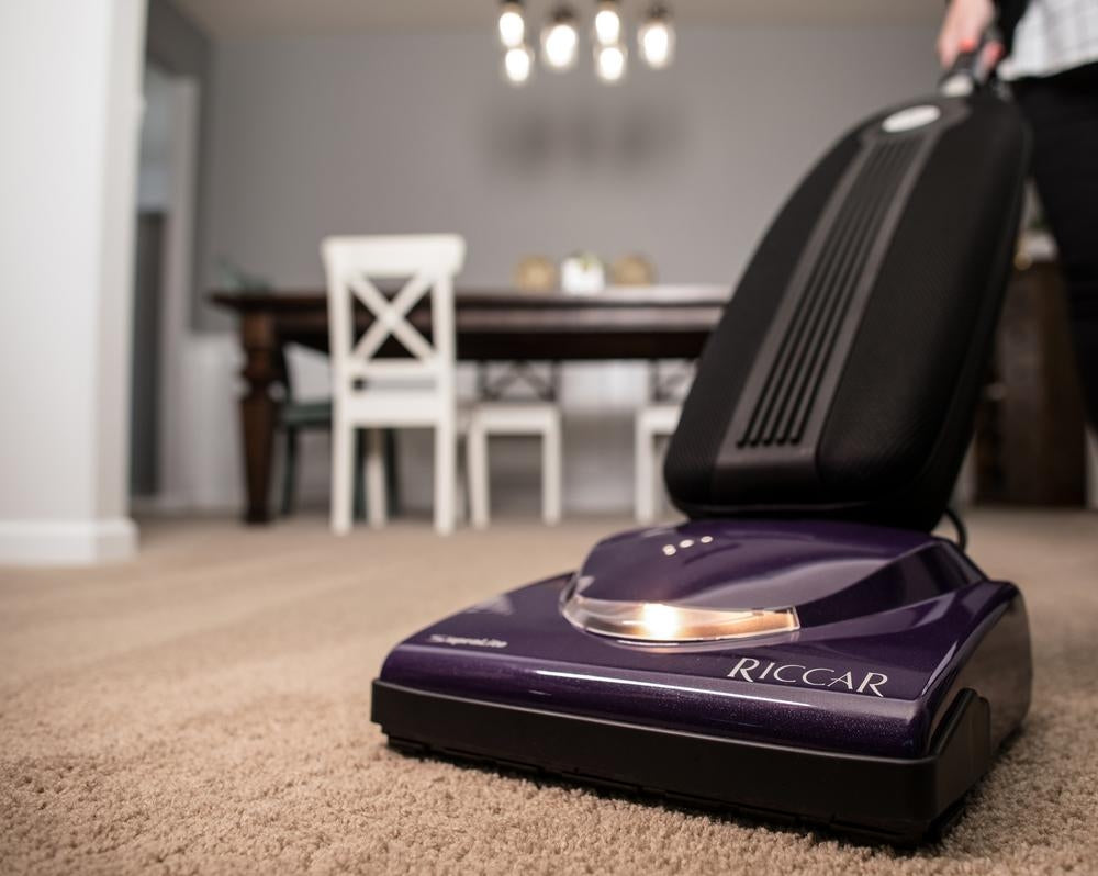 Riccar R10S SupraLite Standard with its headlight on, vacuuming carpet in a dining room